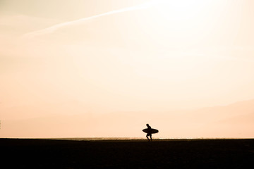 Naklejka na ściany i meble Silhouette of a surfer walking to the sea at sunset. Surfer at santa monica beach los angeles california united states