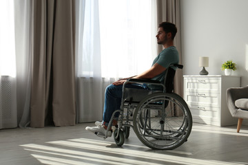 Young man sitting in wheelchair near window indoors