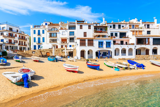 Fishing boats on beach in Port Bo with colorful houses of old town of Calella de Palafrugell in background, Catalonia, Spain