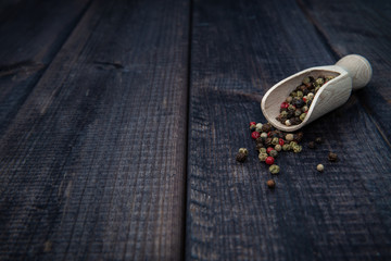 Wooden scoop with black, colorful pepper on a dark wooden table. The concept of using spices for dishes, enriching the taste. Strong, spicy taste.