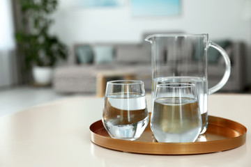 Tray with jug and glasses of water on white table in room, space for text. Refreshing drink