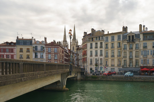 Architecture of city, bridge over river Nive. High medieval cathedral / Gothic facade of Sainte-Marie and residential houses nearby. Touristic concept in Nouvelle Aquitaine.