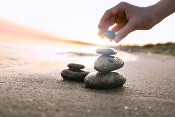 Woman stacking dark stones on sand near sea, space for text. Zen concept