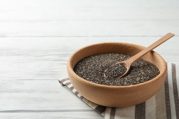 Wooden bowl with chia and spoon on white wooden background, space for text