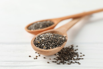 Chia seeds and wooden spoons on white wooden background, copy space