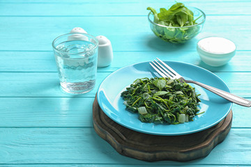 Tasty cooked spinach served on light blue wooden table. Healthy food