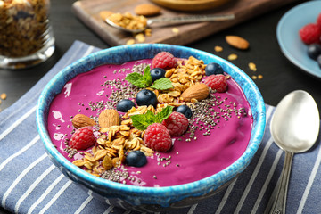Delicious acai smoothie with granola and berries in dessert bowl on table