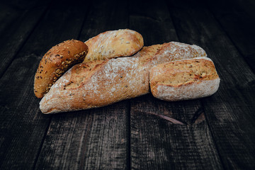 Fresh crisp bread on a dark wooden background. The concept of baking bread, eating meals with rolls, bread. Product made of wheat and rye flour, bread preparation. Eating sandwiches.