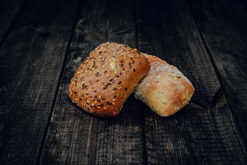 Fresh rolls on a dark wooden background. The concept of baking bread, eating meals with rolls, bread. Product made of wheat and rye flour, bread preparation. Eating sandwiches.