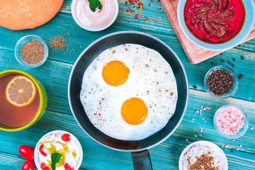 Eggs in Pan with Bread and Hummus and Labneh with Cup of Tea with Limon. On Blue Wood Surface, Perfect Breakfast Meal, Fried eggs in a frying pan