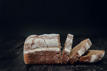 Healthy dark bread and sliced slices on a dark wooden background. The concept of baking bread, eating meals with rolls, bread. Product made of wheat and rye flour, bread preparation.
