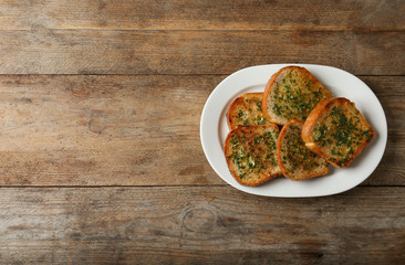 Slices of toasted bread with garlic and herbs on wooden table, top view. Space for text