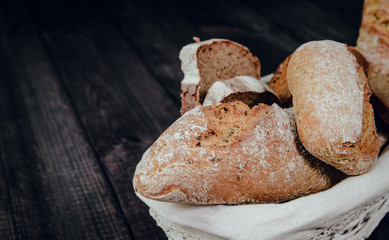 Top view on a basket with bread on a dark wooden background. The concept of baking bread, eating meals with rolls, bread. Product made of wheat and rye flour, bread preparation.