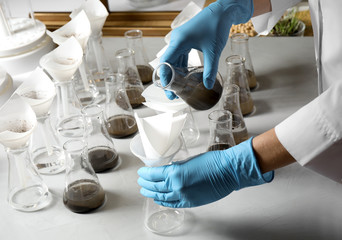 Scientist filtering soil samples at table, closeup. Laboratory analysis