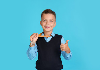 Happy boy in school uniform with golden medal on blue background