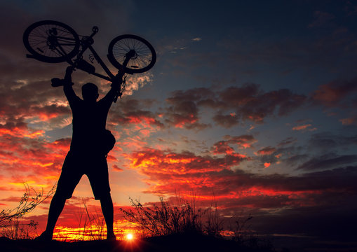cyclist with a bicycle, in the background fiery sunset.