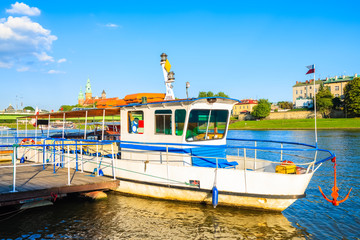 Tourist boat anchoring on Vistula river and Wawel castle in background at sunset time, Krakow, Poland