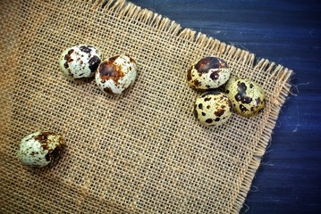 Quail eggs on sackcloth and a black wooden background.