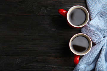 Flat lay composition cups of hot coffee and sweater on black wooden background, space for text. Winter drink
