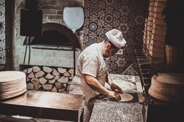 Poster Italian chef in uniform is preparing pastry for pizza at the kitchen. © Fxquadro
