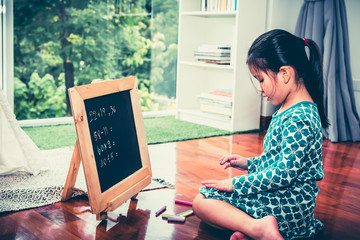 A 6 year old girl are counting fingers to help calculate for practicing math broblems On a small blackboard At her house on vacation, concept to child and education