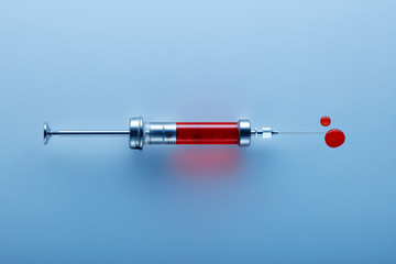 Vintage syringe filled with blood on blue background