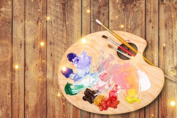 Wooden art palette with blobs of paint and brushes on wooden desk