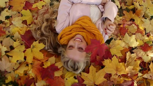 Pretty blonde girl is lying in park on the carpet of yellow maple leaves