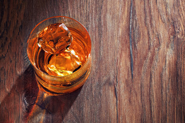 Glass of whiskey with ice on wooden bar table