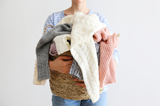 Slim Young Woman Wearing Oversized Cotton Shirt With Blue Stripes & Holding Big Stack Of Folded Knitted Warm Pastel Color Sweaters, Easy Chic Style, Different Knitting Patterns. Background, Copy Space