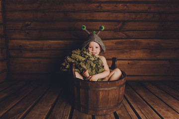 A child with a broom sits in a tub in the bath.