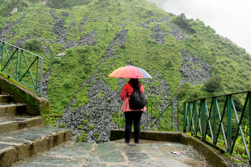 Young indian girl looking towards the beautiful plant covered foggy cloudy hills in himachal pradesh