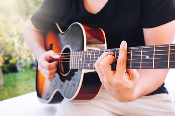 Hands of a young male playing acoustic guitar in the garden