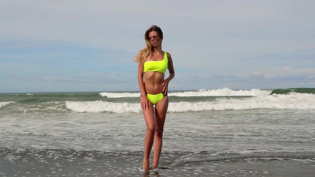 Beautiful young woman in neon yellow bikini swimsuit. Concept of fitness healthy active living. Sport and travel. Weight loss and body image concept. Girl with perfect fit body on tropical beach.