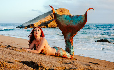 Caucasian redhead woman with mermaid tail reclines on the beach in the waves - 293220506