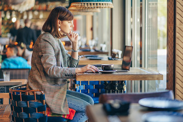 Portrait of a young female freelancer using laptop computer for distance job while sitting in cafe.
