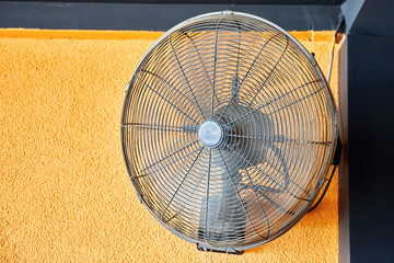 Vintage air cooling fan mounted on a yellow wall blowing air