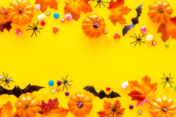 Bright Halloween composition with sweets, bats and pumpkins on yellow background top view frame spac for text
