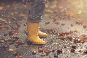 closeup on yellow rubber boots of a child that jumps wildly in a puddle after a rain on an autumn...