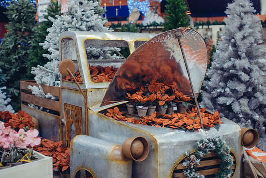New year decoration in shopping center. Vintage car with Christmas flowers in pots - Euphorbia pulcherima surounding with different artificial christmas trees around. Festive mood design. Vintage card
