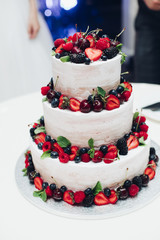 Close-up of a beautiful white cream cheese wedding cake decorated with delicious fresh berries on each layer. Decorated with strawberry, blueberry, cherry and blackberry.
