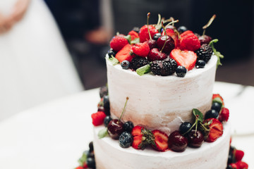 Close-up amazing fresh appetizing sweet cake with cream covered by refreshing fruit and berries. Beautiful serving tasty food brownie on big white plate surrounded by luxury restaurant