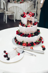Close-up of delicious sweet wedding cake decorated with fresh strawberries, blueberries and blackberries. Sliced wedding cake in close-up.