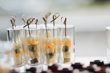Closeup of delicious healthy appetizers served on birthday party. Selective focus of sweet bananas, kiwi, and oranges in glasses. Concept of catering, desserts, arrangement and decoration.