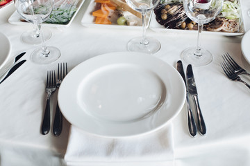 Close-up empty serving white big plate surrounded by knife fork ready to eating food high angle. Beautiful tableware on white tablecloth at luxury fashionable restaurant before dinner