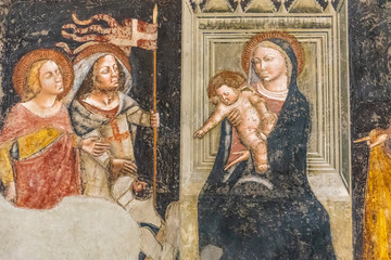 Religious medieval fresco showing Virgin Mary sitting on a throne holding baby Jesus while...