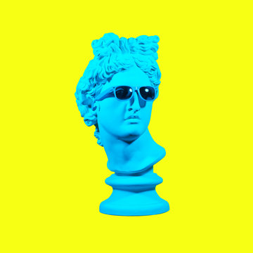 Statue on a yellow background. Gypsum statue of David's head. Creative. Plaster statue of Apollo's head in blue sunglasses. Minimal concept art.