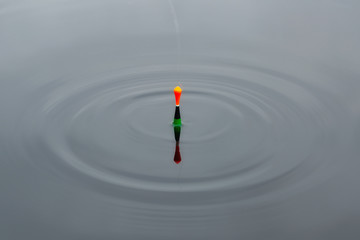 Fishing float floats on the water of the lake making circles in the water. © raland