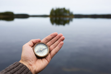 Man holding an old compass in hand. Lake and island on background.