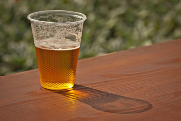 Beer in a plastic glass close-up. Alcoholic beverage at the festival. Bakal on a wooden board.